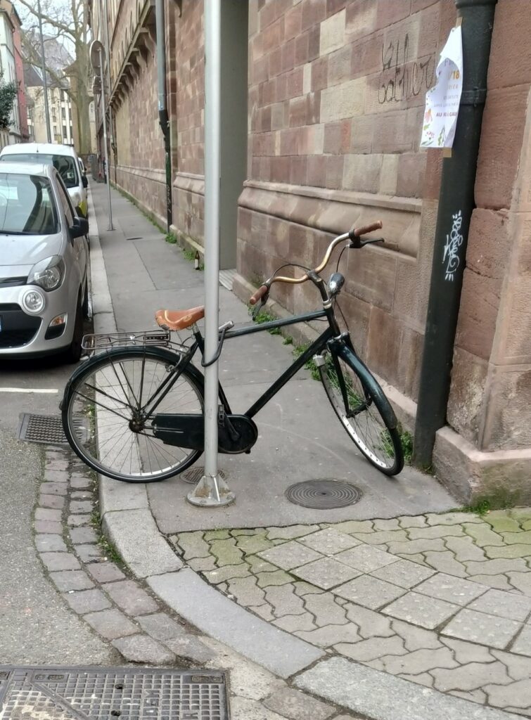 Un vélo attaché à un poteau sur le trottoir bloque le passage des piétons