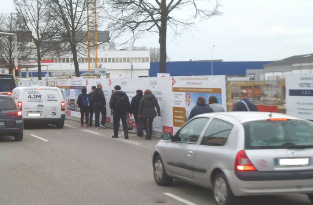 Piétons sur la chaussée longeant des palissades de chantier
